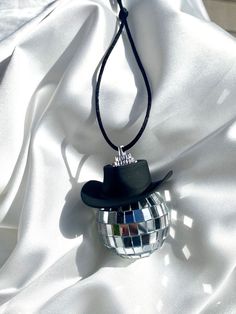 a disco ball with a black hat on it is laying on a white sheet and has a string