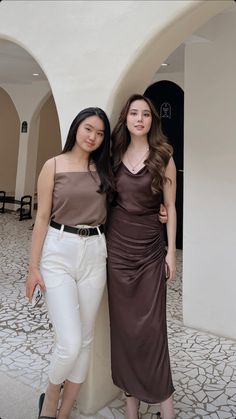 two women standing next to each other in front of a white wall and stone floor