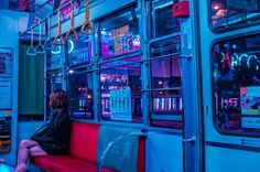 a person sitting on a red bench in front of a blue bus with neon lights