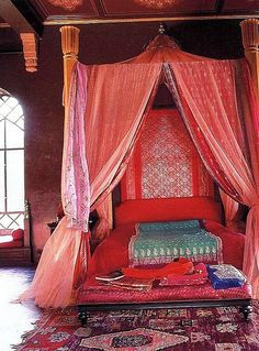 a canopy bed with pink drapes on top of it in a room filled with rugs