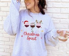 a woman wearing a christmas spirit sweatshirt with wine glasses on her chest and santa hat