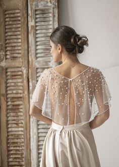 the back of a woman wearing a white dress with pearls on it and sheer sleeves