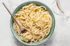 a blue bowl filled with pasta next to a glass of wine on top of a table