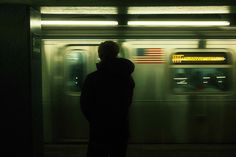 a man standing in front of a subway train at night with the lights on and an american flag painted on it