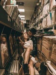 a man and woman sitting on the floor in a room full of record shelves with records