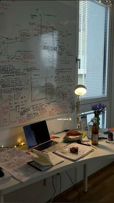 a laptop computer sitting on top of a desk next to a whiteboard covered in writing