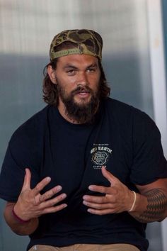 a man with long hair and a beard wearing a black t - shirt holds his hands out in front of him