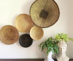 three woven baskets are hanging on the wall above a vase with a plant in it