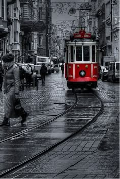 a red trolley car traveling down a street next to tall buildings on a rainy day