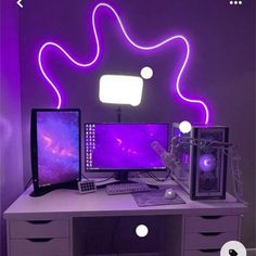 a desk with two computers on it in front of a neon purple wall and white drawers