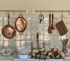 pots and pans are hanging on the wall above a sink with flowers in it