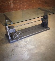 a glass and metal table with wheels on the bottom, in front of a brick wall