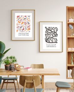 two framed art prints hang on the wall above a dining room table with blue chairs