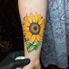 a sunflower tattoo on the arm with green leaves and yellow flower in it's center