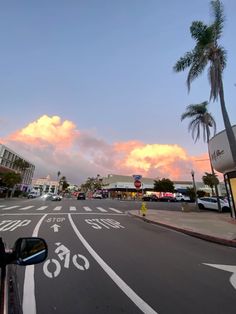 an empty street with palm trees on both sides and buildings in the background at sunset