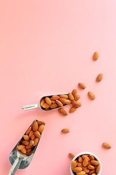 two spoons filled with almonds on top of a pink surface