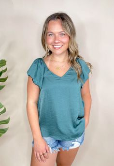 Get ready to elevate your workwear with the Abena Flutter Sleeve Blouse! This classic style blouse features a v-neck front and back keyhole closure. The flutter ruffle sleeves make it the perfect addition to any wardrobe. Unlined. Dress it up or down for a versatile and stylish look. Flowy V-neck Top For Work, Versatile Short Sleeve V-neck Top For Work, Feminine Green V-neck Top, Flowy V-neck Top For Workwear, Chic Solid Top With Notched Neckline, Flowy Solid Color V-neck Blouse, Flowy Solid V-neck Blouse, Solid Color Flowy V-neck Blouse, Chic Flowy Blouse With Split Neck