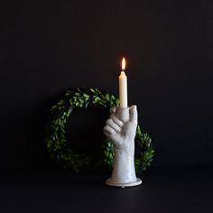 a hand holding a lit candle in front of a wreath