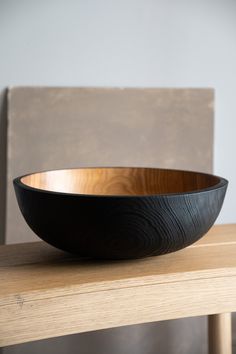 a wooden bowl sitting on top of a wooden table next to a chair and wall