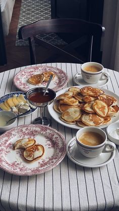 a table topped with plates of food next to cups of coffee and saucers on top of a table