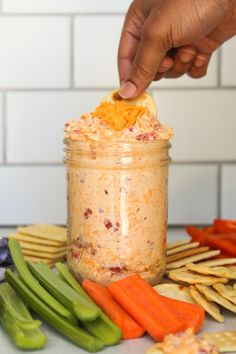 a person dipping something into a jar with carrots, celery and crackers