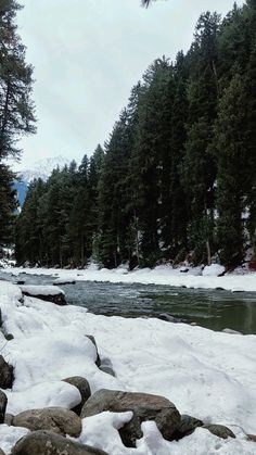 a river surrounded by snow covered rocks next to pine trees and evergreens in the background