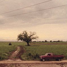 a red truck parked on the side of a dirt road next to a green field