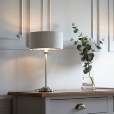 a vase with flowers on a table next to a lamp and drawers in a room