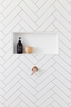 a white shelf with two wooden spoons and a black bottle on it, in front of a herringbone pattern wall