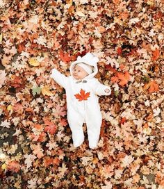 a baby is laying in the leaves with his arms up and head down on it's back