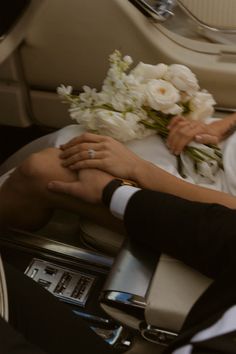 the bride and groom are holding hands while sitting on an airplane seat with flowers in their lap