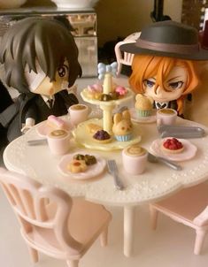 two figurines sitting at a table with pastries on it and one is eating