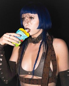 a woman with blue hair and makeup drinking from a drink bottle while wearing leather clothes