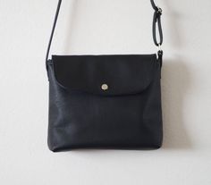 "This small crossbody bag features soft black leather with fabric lining, an adjustable shoulder strap, and a magnetic closure. Details: -Dimensions: 7\" length (top to bottom), 8\" bottom width (side to side), 3\" depth, 8\" X 3\" base (bottom) -Shoulder strap measures approx. 45-50\" total (adjustable) -Navy interior lining -Internal pocket -Magnetic closure Because each bag is made by hand, the measurement is approximate and may vary slightly from one bag to another. Options: #1 Vegan (fake) Black Soft Leather Crossbody Flap Bag, Versatile Black Flap Bag In Soft Leather, Crossbody Flap Bag With Fold Over Clasp, Everyday Crossbody Flap Bag With Fold Over Clasp, Everyday Crossbody Flap Bag With Fold-over Clasp, Black Soft Leather Crossbody Saddle Bag, Versatile Black Flap Bag, Black Crossbody Flap Bag With Adjustable Strap, Black Shoulder Bag With Adjustable Strap And Flap