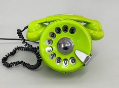 an old fashioned green phone with black and silver buttons on the dial, sitting on a white surface