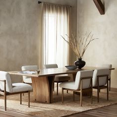 a dining room table with chairs and a vase on top of it in front of a window