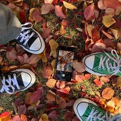 two pairs of shoes are laying on the ground with autumn leaves surrounding them and a cell phone