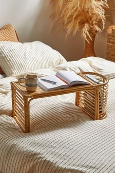 a coffee table with a book and cup on it in front of a white bed