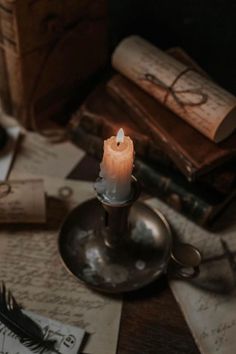 a lit candle sitting on top of a table next to some old books and papers