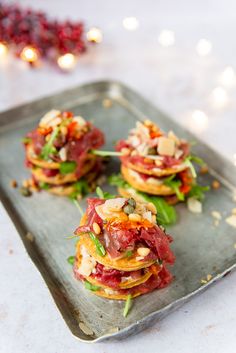 small appetizers with meat and vegetables on a metal tray next to christmas lights