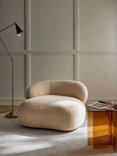 a living room with a chair, table and lamp on the floor in front of a wall