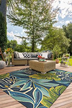 an outdoor area with furniture and flowers on the floor, in front of a wooden deck