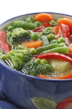 a blue bowl filled with broccoli, carrots and peppers