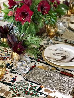 the table is set with red flowers and place settings