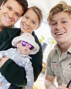 two men and a woman are smiling for the camera with a baby in their arms