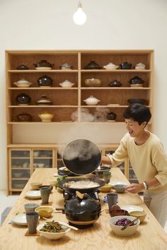 a woman standing in front of a table filled with pots and pans on top of it