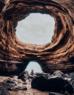 a person sitting in the middle of a large rock formation with a hole cut into it