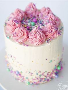 a white cake with pink frosting and sprinkles on the top is sitting on a plate