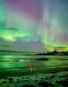 a person standing on the beach with their arms in the air under an aurora bore