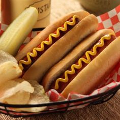 two hotdogs with mustard and ketchup in a basket next to pickles